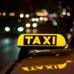 Yellow and black sign of Taxi placed on top of a car at night